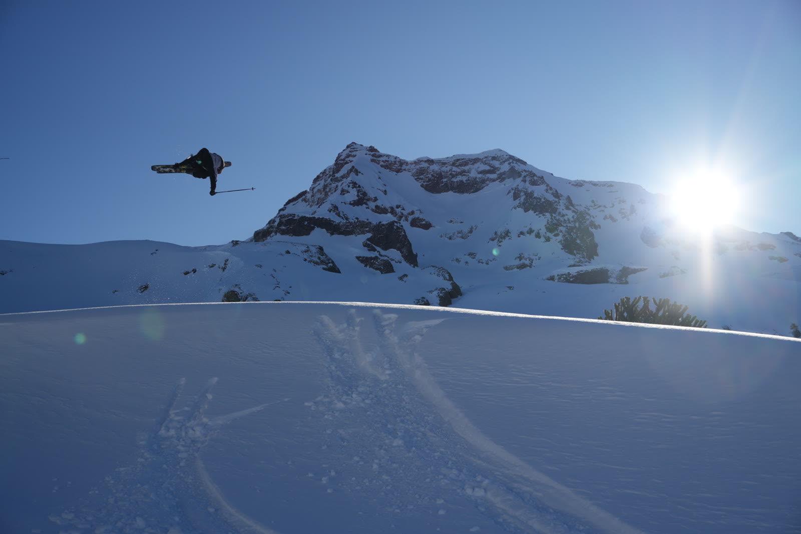 Salto de snowboard con destello de sol y cumbre nevada
